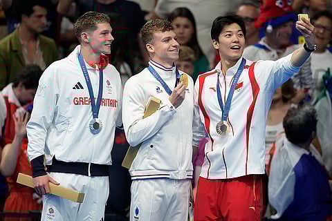 Gold medalist Leon Marchand, centre stands with silver medalist Duncan Scott and bronze medalist Shun Wang